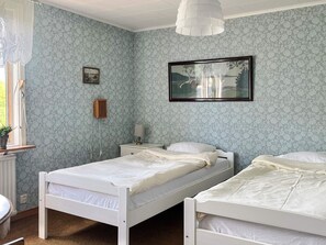 A room with two single beds, a small bedside table with a lamp, a framed picture on the wall, and a window with a curtain. - 5 Person Holiday Home in Gunnebo (Gunnebo)