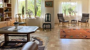 Ett vardagsrum med en soffa, stolar, ett bord och ett fönster med växter.