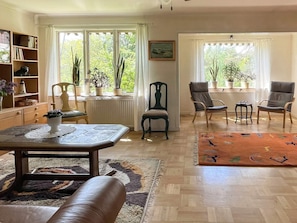 A living room with a sofa, chairs, a table, and a window with plants.