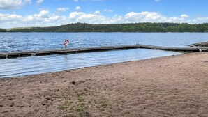 En sjö med en träbrygga som sträcker sig ut i vattnet, omgiven av en sandstrand.