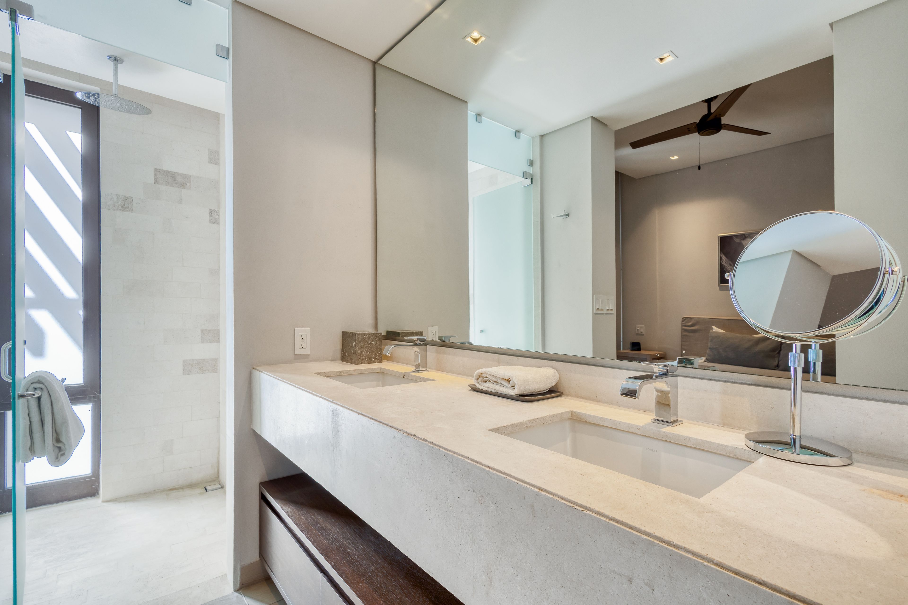 A modern bathroom with a large mirror, two sinks, and a shower area.