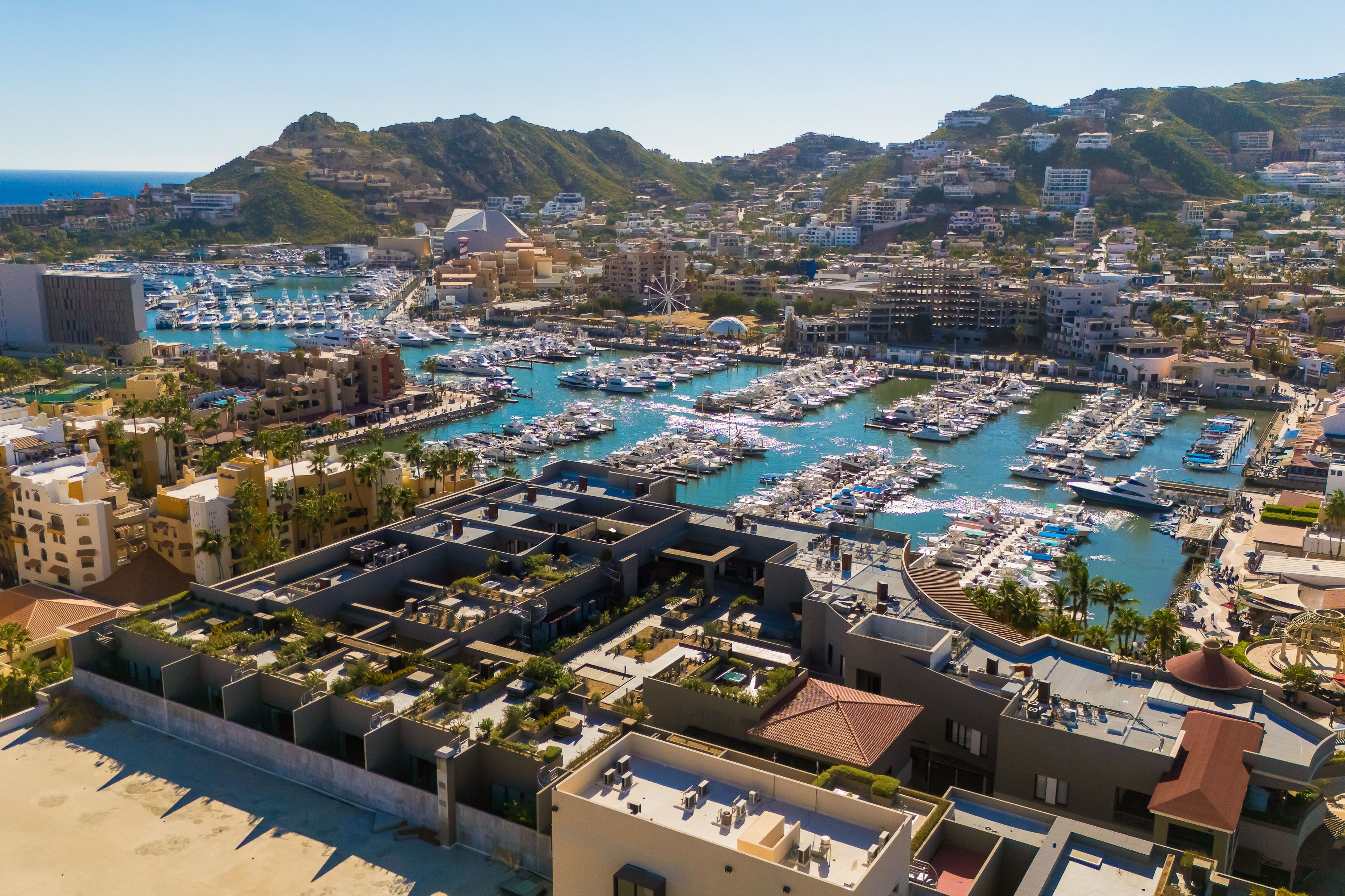 A marina with numerous boats docked, surrounded by residential buildings and hills in the background.
