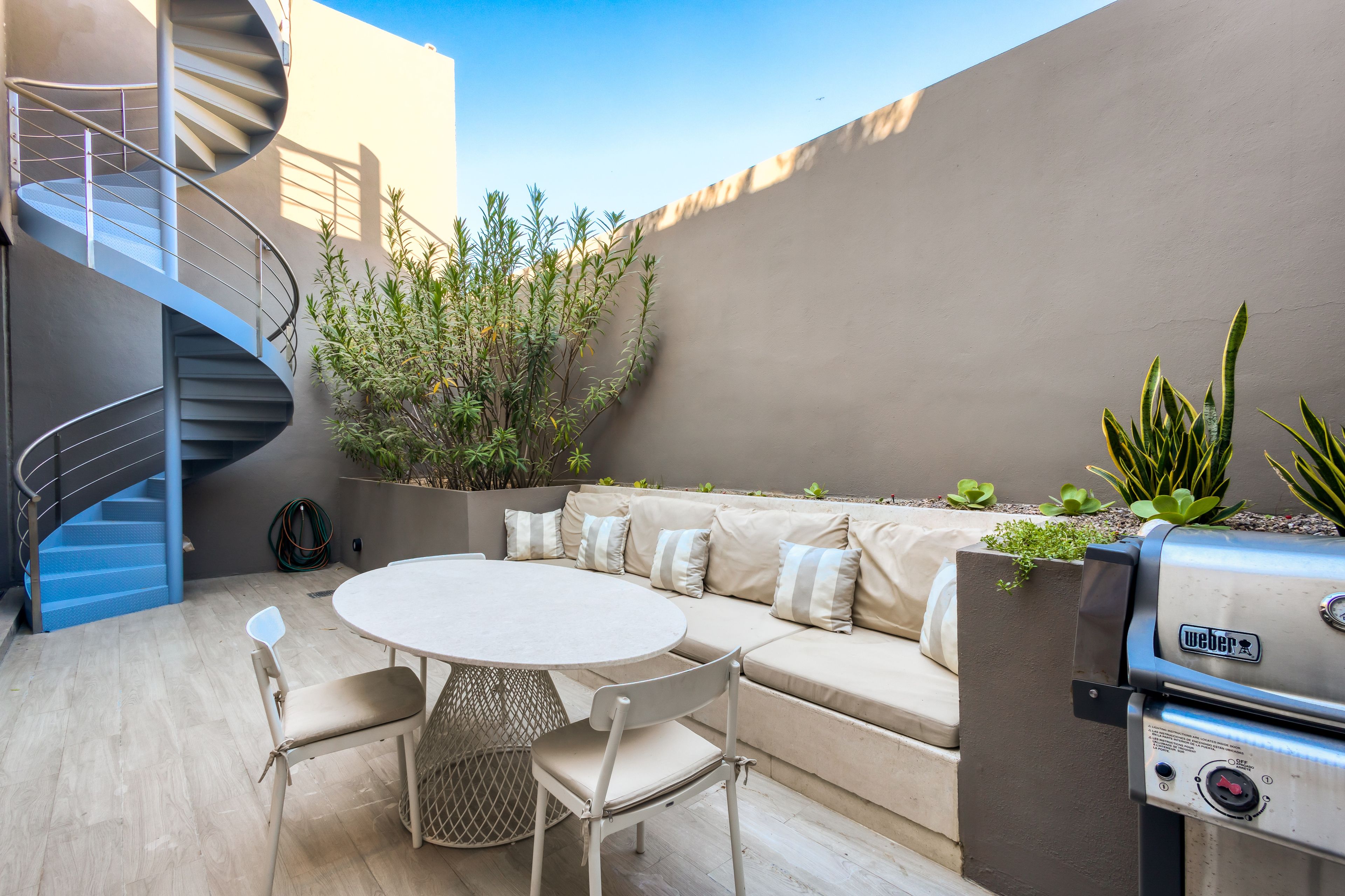 Eine moderne Außenpatio mit Wendeltreppe, einem runden Tisch mit Stühlen, einer eingebauten Sitzecke und einem Weber Grill.