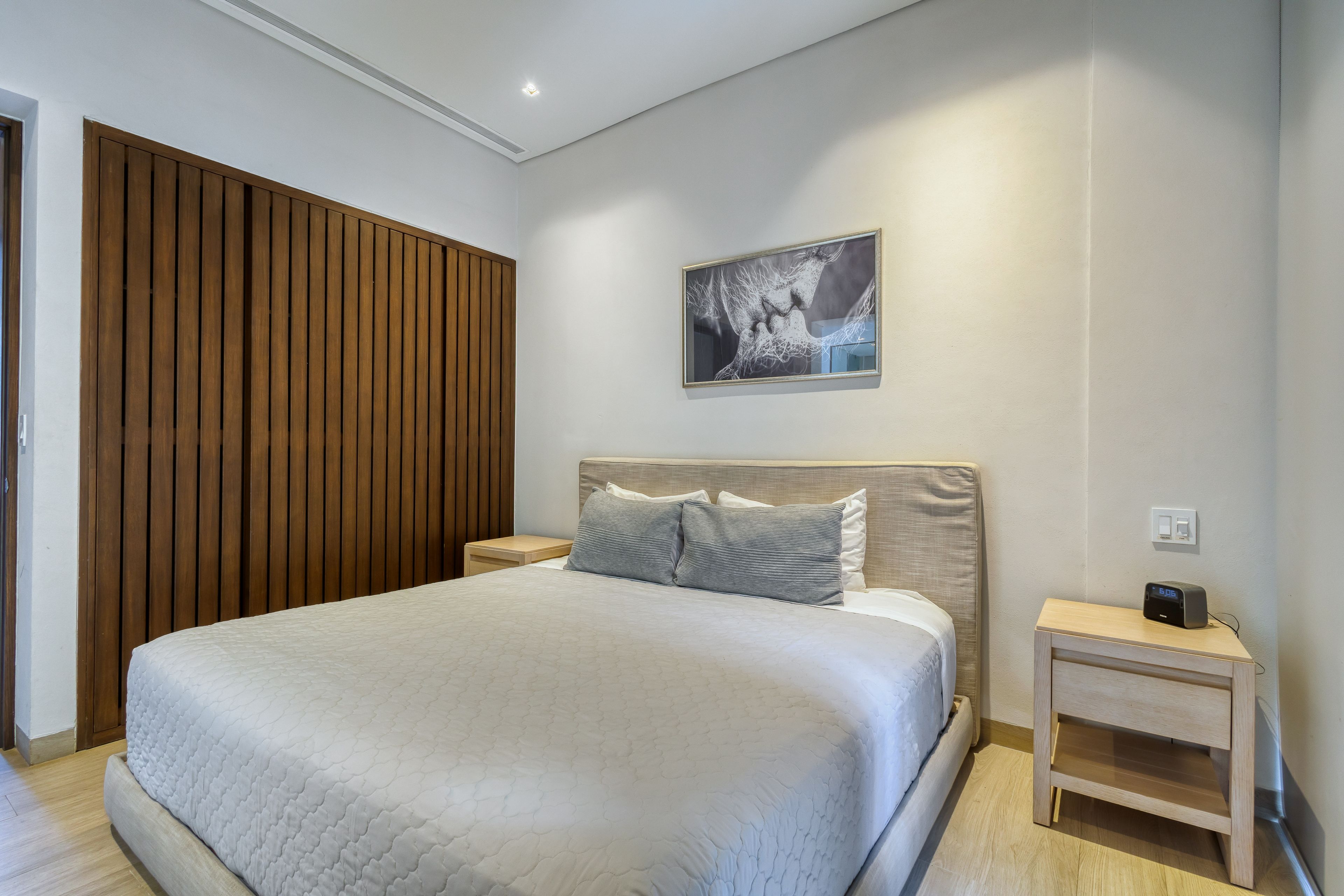 Une chambre à coucher bien am énagée, avec un grand lit, un mur recouvert de panneaux de bois, une œuvre d’art encadrée et une table de chevet avec une horloge.
