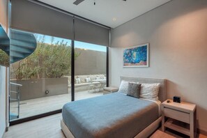 Un dormitorio con cama, mesita de noche, un cuadro y puerta corrediza de vidrio que da a una zona de estar exterior.