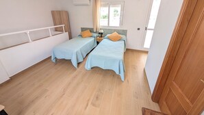 Camera da letto con due letti, una ventola a soffitto, un condizionatore d'aria, una finestra con tende e pavimento in legno.