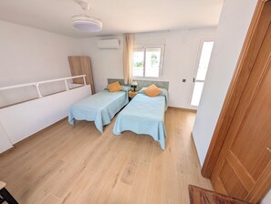 A bedroom with two beds, a ceiling fan, an air conditioning unit, a window with curtains, and a wooden floor. - Luminous Duplex centrally located in Arroyo de la Miel, 3 minutes from downtown. (Benalmádena)