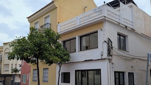 Un edificio a più piani con balconi, un albero sullo sfondo e una strada di fronte.