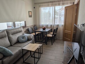 A living room with a sofa, a small table, a dining table with chairs, a TV, and a window with curtains. - Luminous Duplex centrally located in Arroyo de la Miel, 3 minutes from downtown. (Benalmádena)