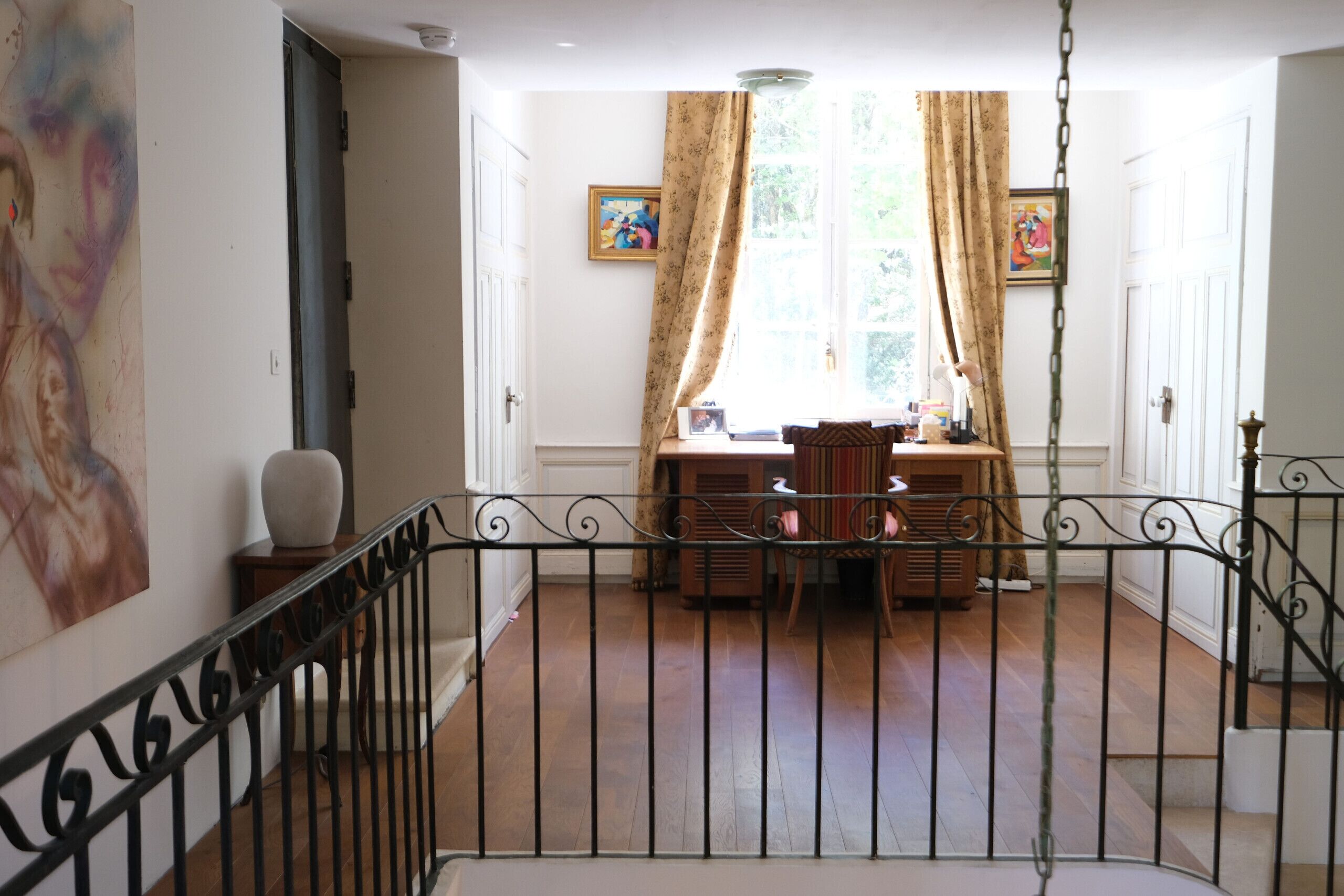 A room with a wooden floor, a dining table with chairs, a hanging light fixture, and a window with curtains.