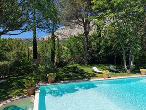 Ein Swimmingpool mit Liegestühlen, umgeben von Bäumen und einer Bergkulisse.