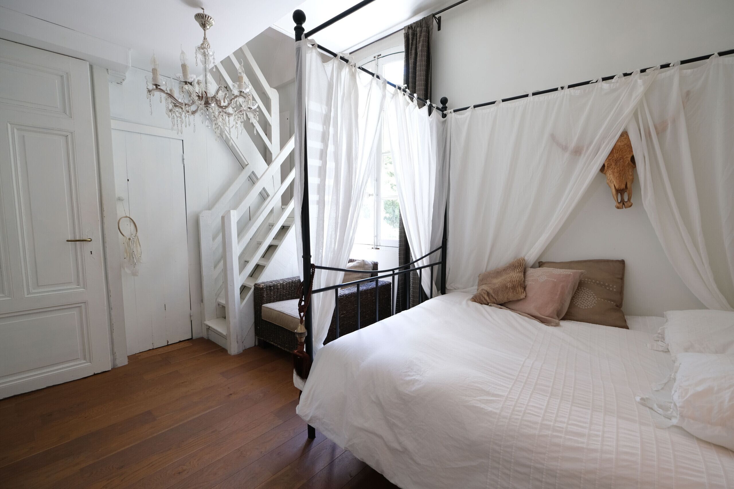 A bedroom with a four-poster bed, a staircase, and a chandelier.