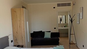 A bedroom with a bed, a black sofa, a wooden door, a small table, and a mirror.