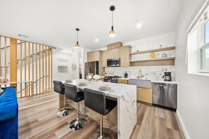 Cozinha moderna com ilha central, banquetas, eletrodomésticos de aço inoxidável e escada de madeira.