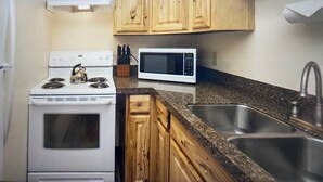 A kitchen with wooden cabinets, a white stove, a microwave, and a stainless steel sink.