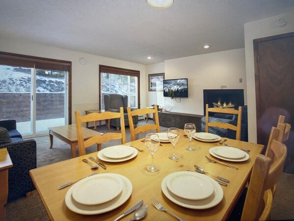 A dining area with a table set for four, chairs, a television, and a fireplace.