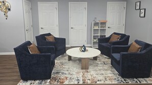 Une pièce avec quatre fauteuils bleu foncé, une table basse ronde et une porte blanche à l’arrière-plan.