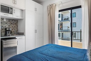 Une chambre d’hôtel avec un lit, une kitchenette et un balcon donnant sur l’immeuble.