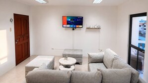 Una sala de estar moderna con un sofá gris, una mesa de centro redonda y un televisor de pantalla plana montado en la pared.