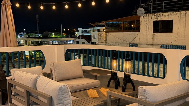 Una terraza en la azotea con mobiliario exterior, luces colgantes y vistas a la ciudad.