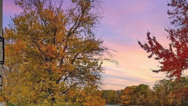 A deck with outdoor seating and a table, overlooking a body of water with autumn foliage. - Luxury Lakehouse on the water! (Tully)