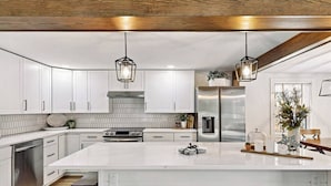 A modern kitchen with white cabinetry, a large island, stainless steel appliances, and pendant lighting. - Luxury Lakehouse on the water! (Tully)