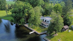 A house with a dock extending into a lake, surrounded by trees and a grassy area. - Luxury Lakehouse on the water! (Tully)