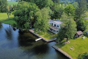 Ein Haus mit einem Steg, der in einen See ragt, umgeben von Bäumen und einer Rasenfläche.