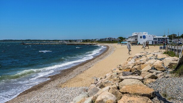 Une plage bordée d’une côte rocheuse, avec une jetée et un bâtiment orné du logo bleu de la NASA.