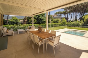 Una terrazza esterna con tavolo e sedie in legno, una piscina e vista sul paesaggio circostante.