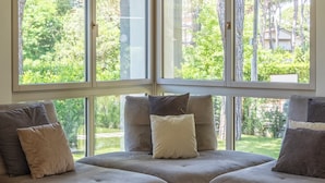 A corner seating area with a sofa and ottoman, large windows, and a view of greenery. - Villa Smeralda (Marina di Pietrasanta)