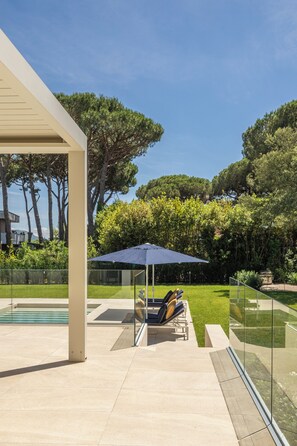 A poolside area with a glass enclosure, a lounge chair, and a blue umbrella.
