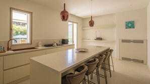 A modern kitchen with a large island, bar stools, pendant lights, and a view of the outdoors. - Villa Smeralda (Marina di Pietrasanta)
