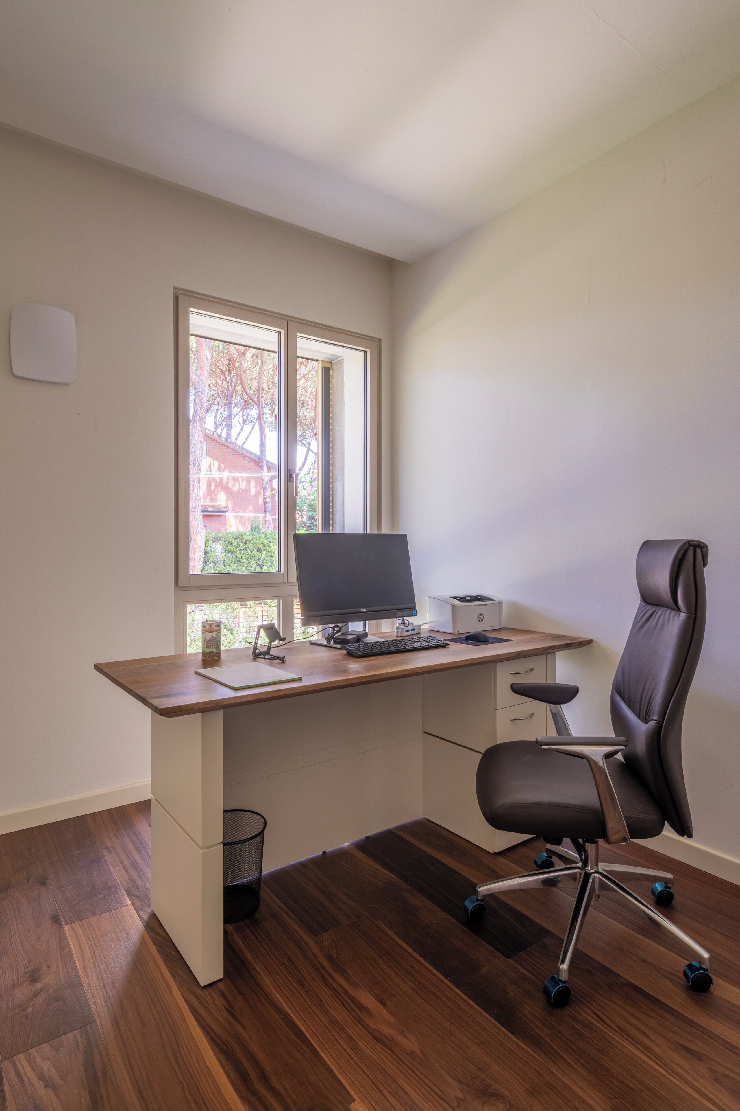 A modern office space with a wooden desk, a black office chair, a desktop computer, and a printer.