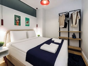 A modern hotel room with a neatly made bed, a bedside table with a plant, a wall-mounted shelf with clothes, and two framed pictures. - 5 min Walk to Taksim Square & Galata Sleeps 6 (Istanbul)