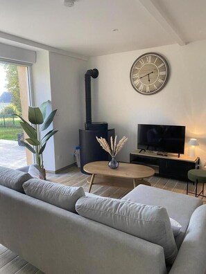 A modern living room with a sofa, a TV, a fireplace, and a clock on the wall. - GITE DES MARES - VILLERS-SUR-LE-MONT (VILLERS-SUR-LE-MONT)