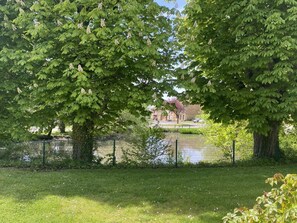 A park with trees, a pond, and a building in the background. - GITE DES MARES - VILLERS-SUR-LE-MONT (VILLERS-SUR-LE-MONT)