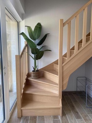 A wooden staircase with a potted plant on the landing, leading to a room with a large window and a metal rack. - GITE DES MARES - VILLERS-SUR-LE-MONT (VILLERS-SUR-LE-MONT)
