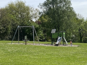 Ein Spielplatz mit Schaukel, Rutsche und Klettergerüst in einem grünen Park.