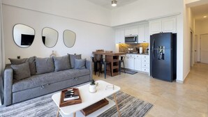 A modern kitchen with white cabinets, a black refrigerator, and a dining area with a wooden table and chairs. - Stylish Coastal Retreat With Breathtaking Views, Resort Pool & Private Balcony (Cabo San Lucas)