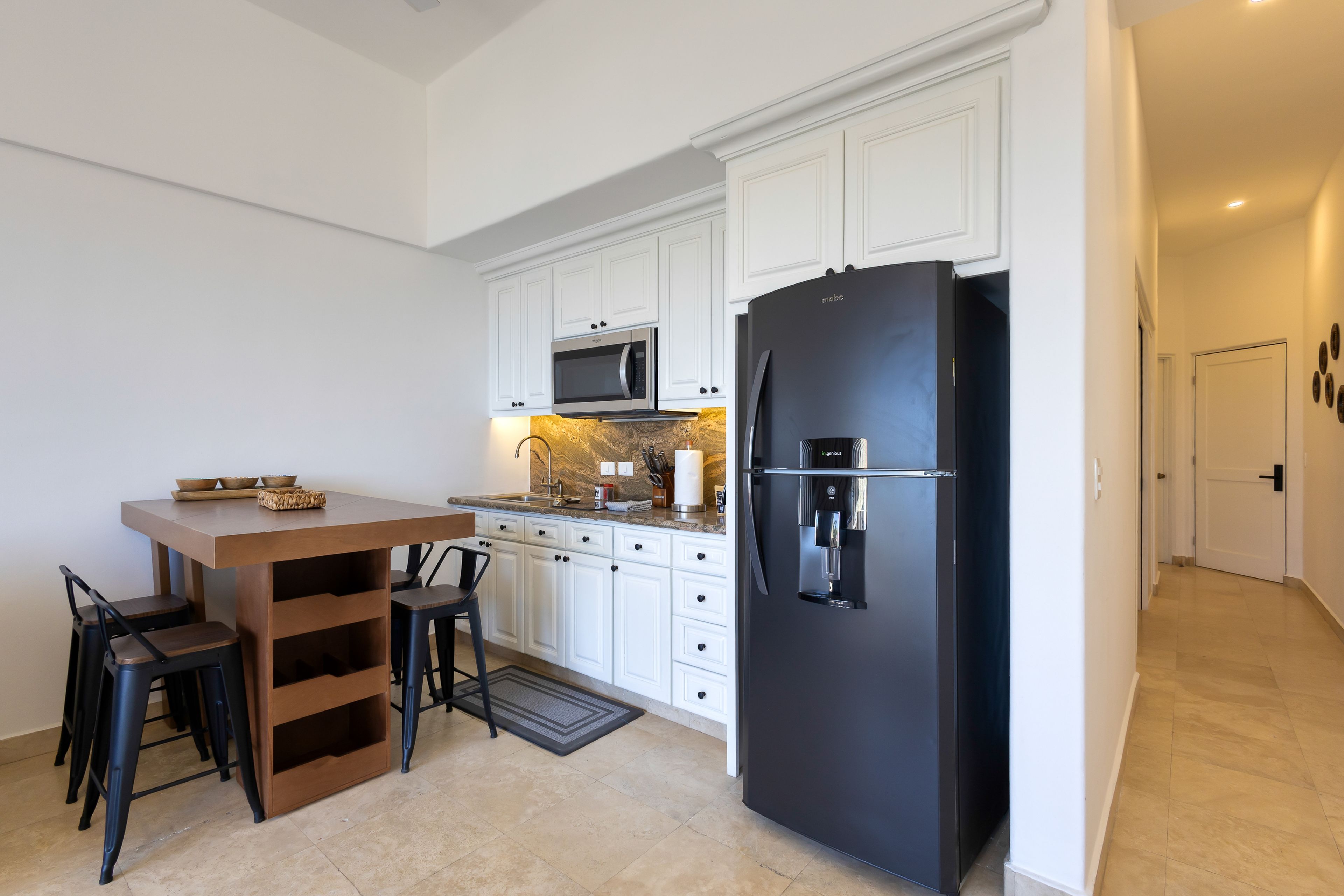 Une cuisine moderne avec des meubles blancs, un réfrigérateur noir, un four à micro-ondes et une table à manger en bois, accompagnée de chaises.