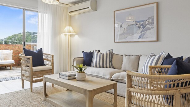 Una sala de estar moderna con muebles de mimbre, una mesa de centro de madera y un amplio ventanal con vistas a la vegetación.