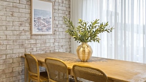 Un comedor con pared de ladrillo, un cuadro enmarcado, un jarrón con follaje y una mesa de madera con sillas de mimbre.