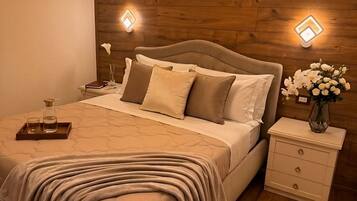 A bedroom with a wooden headboard, a bed with beige bedding, bedside tables with lamps, and a nightstand with a vase of flowers.