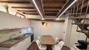 A compact kitchen with a wooden table, white chairs, a built-in stove, and a hanging light fixture. - Terme house (Bagni San Filippo)