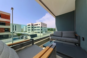 Ein Balkon mit einer Couch, einer Glastrennwand und Blick auf moderne Gebäude.