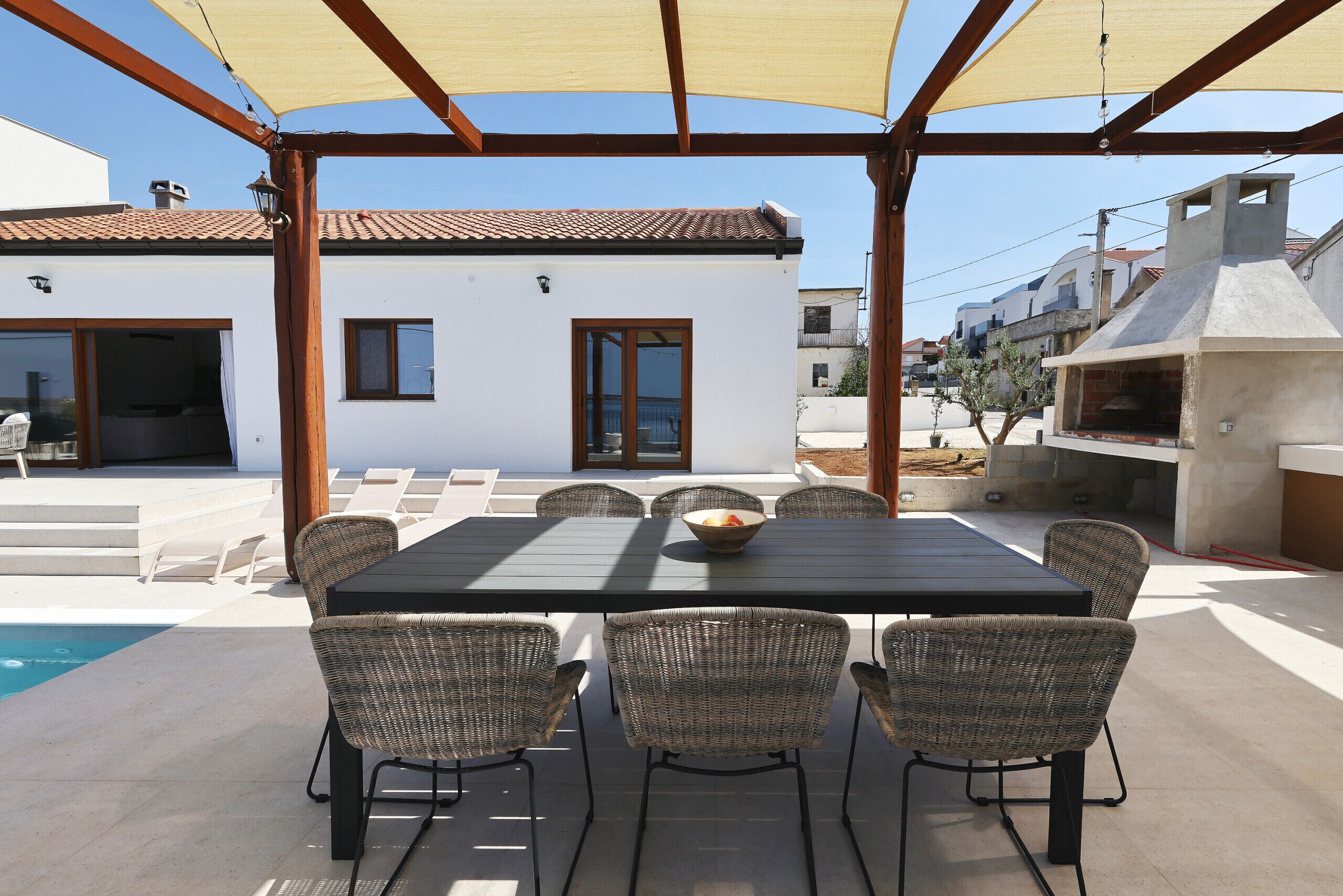 Un espace extérieur abrité, aménagé pour les repas, avec une piscine, des chaises en osier et une table.