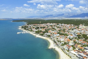 Luftaufnahme einer Küstenstadt mit Häusern, einem Strand und Bergen im Hintergrund.