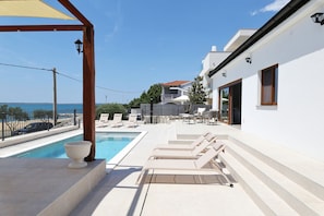 Ein Poolbereich mit Liegestühlen und Blick auf das Meer.