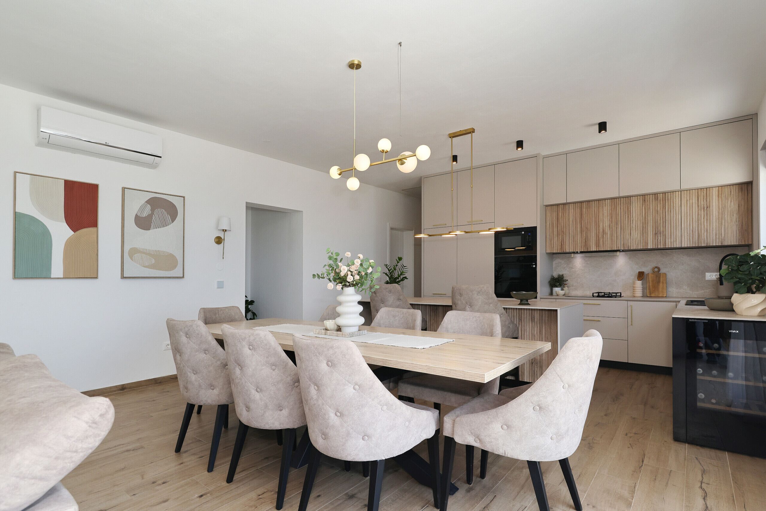Une cuisine moderne avec un coin repas, comprenant une table en bois, des chaises rembourrées, un luminaire suspendu et des placards intégrés.